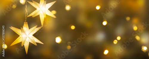 hanging shiny christmas stars on bright golden background, festive decoration for christmas eve, greeting card concept with copy space