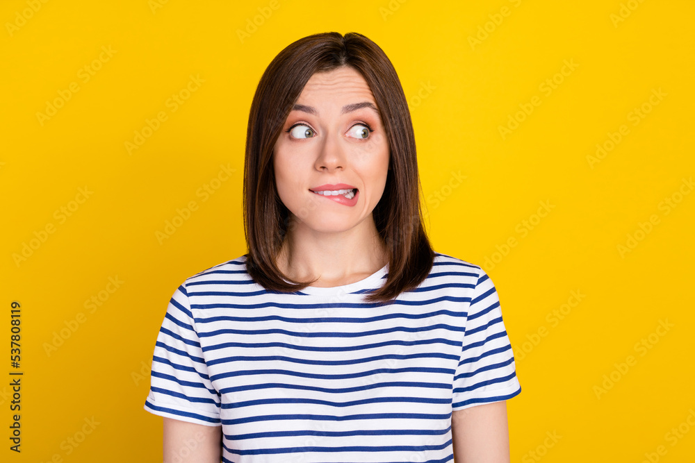Photo of young gorgeous funny lady wear striped blue t-shirt bite lips look empty space oops fail isolated on yellow color background Photo of young gorgeous funny lady wear striped blue t-shirt bite lips look empty space oops fail isolated on yellow color background