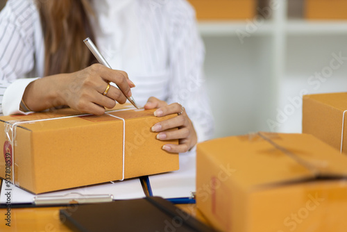 Woman in a small start-up business woman working in a home office working on a laptop and smartphone checking orders from the internet in preparation for shipping.