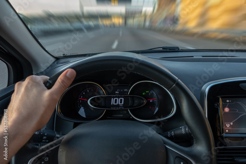 Driver view to the speedometer at 100 kmh or 100 mph and the road blurred in motion, view from inside a car of driver POV of the road landscape.