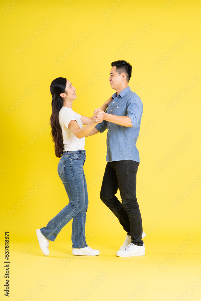 full body image of asian couple posing on yellow background