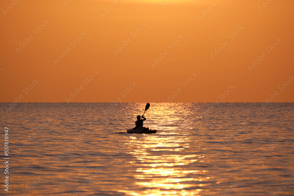 Dark silhouette of lonely fisherman rowing on his boat on sea water at sunset