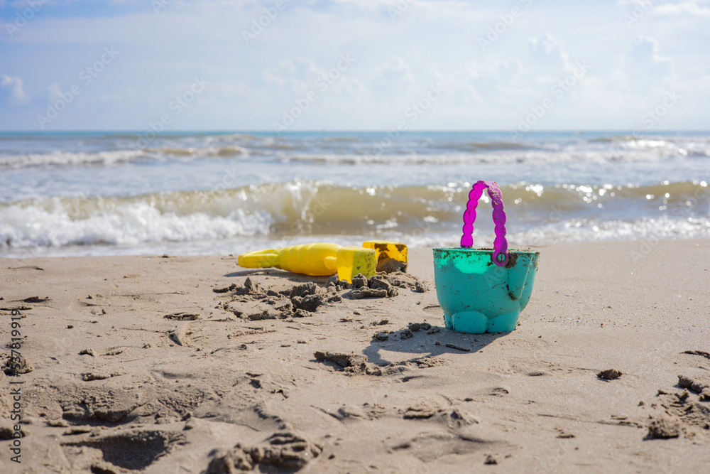 Beach in Valencia, Spain, Port Saplaya, where you can see a plastic green and purple  bucket in the sand, a yellow  gripper, and some waves in the Mediterranean sea