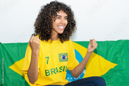 Cheering brazilian female soccer fan with flag of Brazil watching game on tv