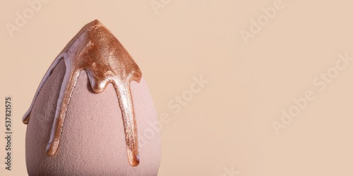Closeup photography of beauty blender with dripping bronzer on it.Neutral beige background,large banner with copy space.