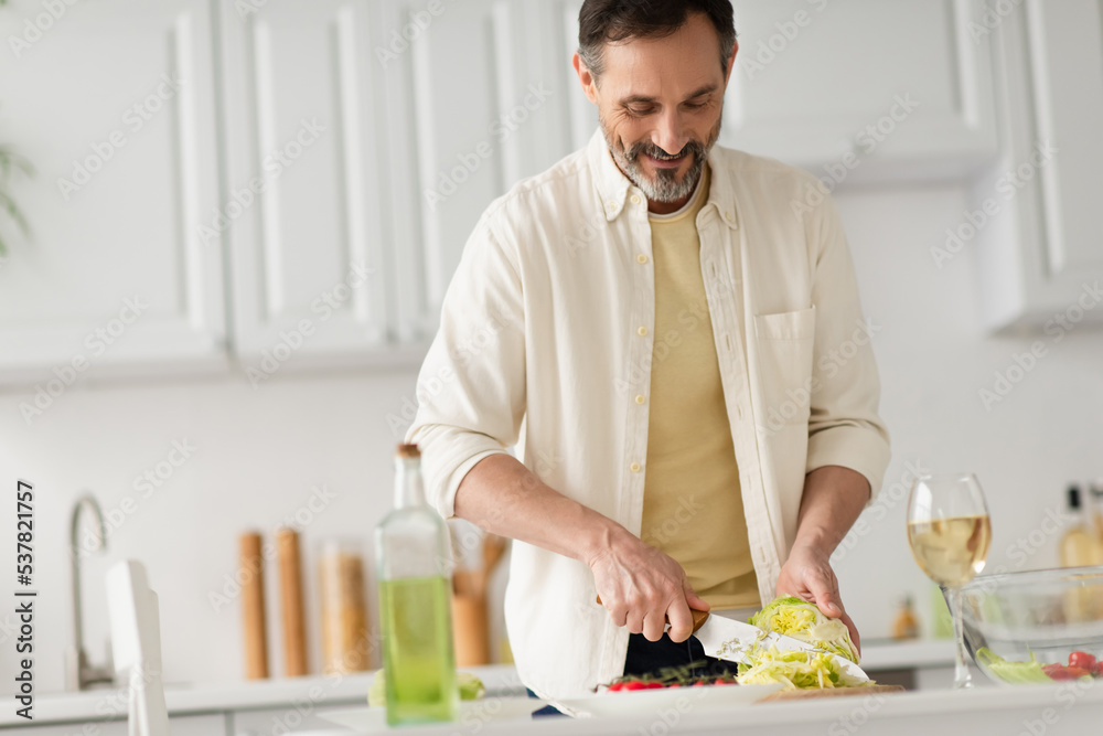 happy bearded man cutting lettuce near bottle with oil and glass of white wine. happy bearded man cutting lettuce near bottle with oil and glass of white wine.