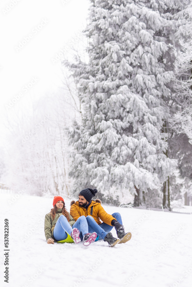 Couple having fun sliding down the hill in the snow while on winter vacation