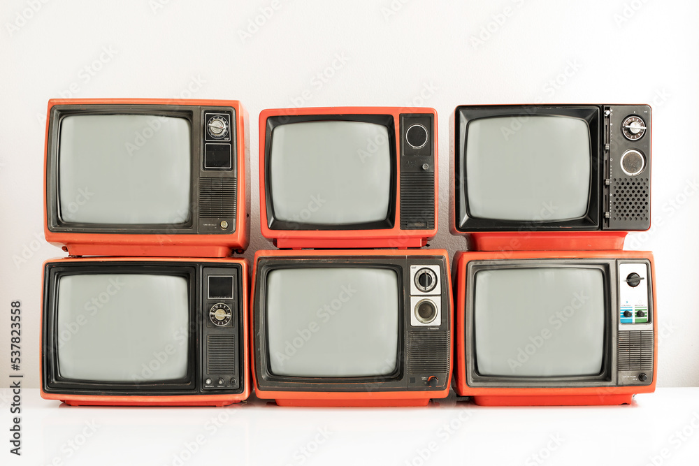 Pile of old red retro televisions with blank gray screen in room. Six old vintage tube TVs on
