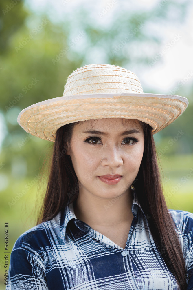 Portrait of a beautiful young asian farmer girl in plaid shirt and hat looking at the camera.