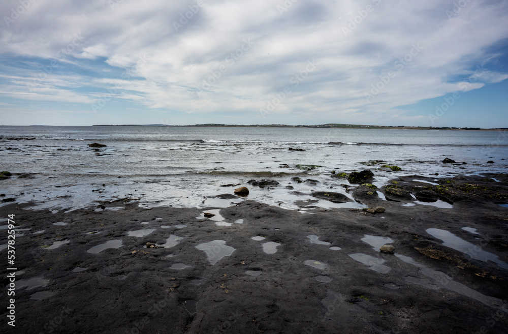 A storm has washed away the sand on a beach in co. Mayo, Ireland. Only black peat now remains. Here and there stumps emerge, called bog oak, remnants of a forest long ago.