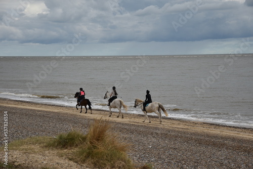 People horse riding on the beach with a cloudy sky background. Taken in Lowestoft England. 