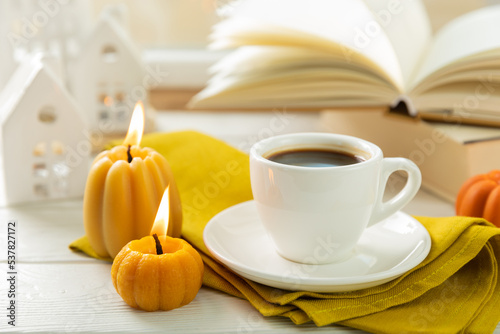 Autumn composition, a cup of hot coffee, a decorative little house, pumpkin candles, books and a warm sweater on a wooden table. Seasonal morning hot coffee. Cozy interior decor