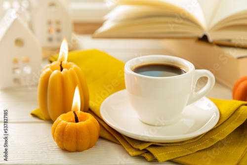 Autumn composition, a cup of hot coffee, a decorative little house, pumpkin candles, books and a warm sweater on a wooden table. Seasonal morning hot coffee. Cozy interior decor