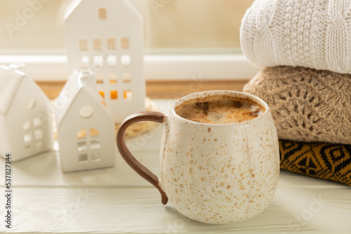 Winter.Winter composition, a cup of hot coffee, a decorative small snow-covered house and a warm sweater on a wooden table.Seasonal morning hot coffee.Merry Christmas and Happy New Year!Cozy interior