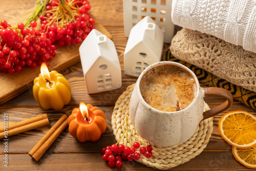 Autumn composition, a cup of hot coffee, a decorative little house, pumpkin candles, books and a warm sweater on a wooden table. Seasonal morning hot coffee. Cozy interior decor