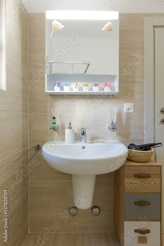 Bright bathroom with large beige tiles. Front view of sink with mirror above