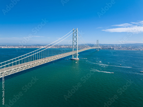 Small boats sail under long suspension bridge on sunny day