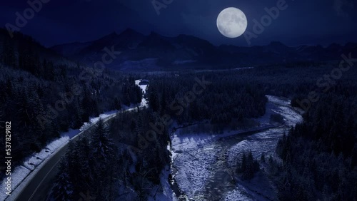 Mountains at winter night, aerial view. Magical white winter and big shining moon. Unspoiled winter scenery. Mountain twisted road at night, alpine epic view.