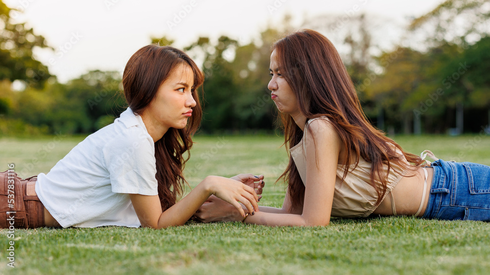 Young beautiful asian girl enjoying themself in the park. They are lying on the green grass leaning into each other while having a good time. Young beautiful asian girl enjoying themself in the park. They are lying on the green grass leaning into each other while having a good time.
