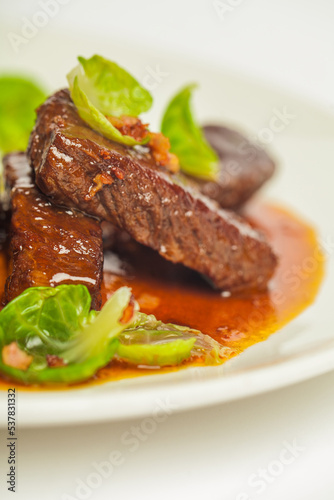 Delicious veal cheeks in red sauce with green. Closeup on a white plate on white background