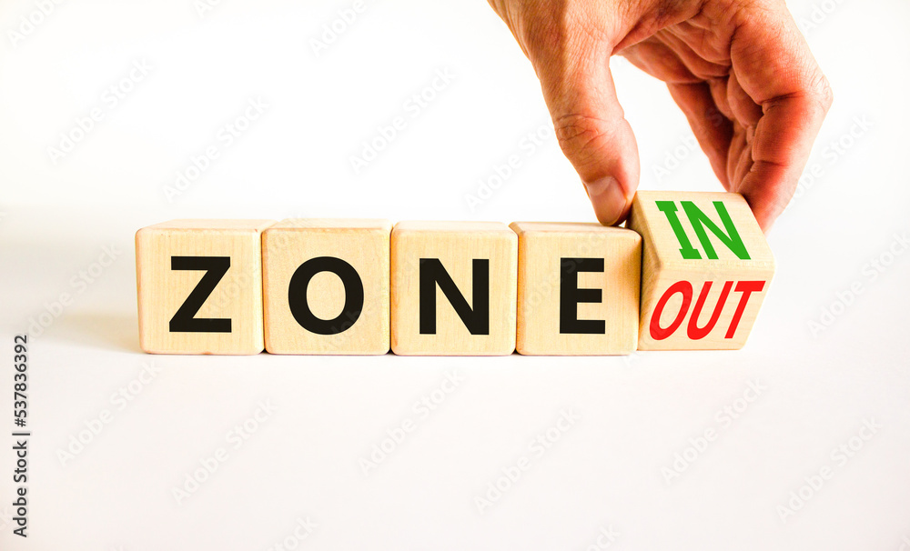 Zone in or out symbol. Concept words Zone in and Zone out on wooden cubes. Beautiful white table white background. Businessman hand. Business zone in or out concept. Copy space. Zone in or out symbol. Concept words Zone in and Zone out on wooden cubes. Beautiful white table white background. Businessman hand. Business zone in or out concept. Copy space.