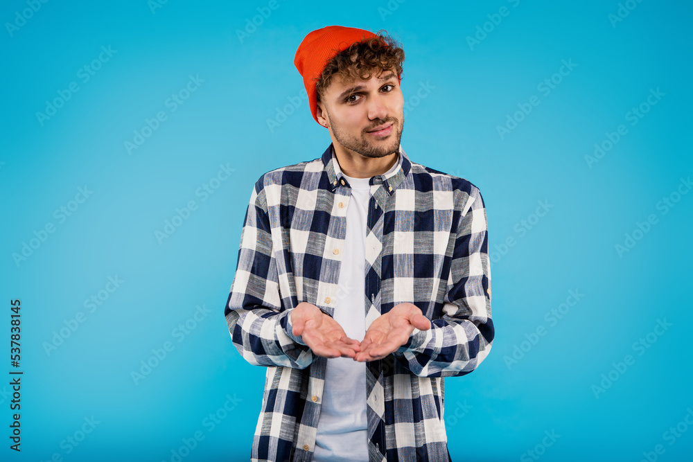 Young attractive smiling man in printed shirt and orange hat looks happy standing on blue background Young attractive smiling man in printed shirt and orange hat looks happy standing on blue background
