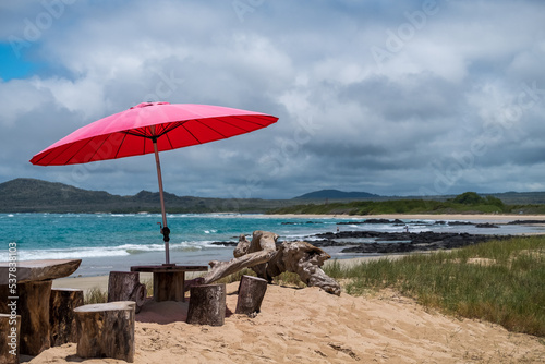 A red umbrella providing shade for people on the beach in Galapagos Islands, Ecuador