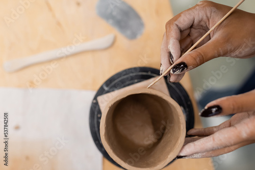 Top view of african american craftswoman making ceramic product with wooden stick in pottery studio.
