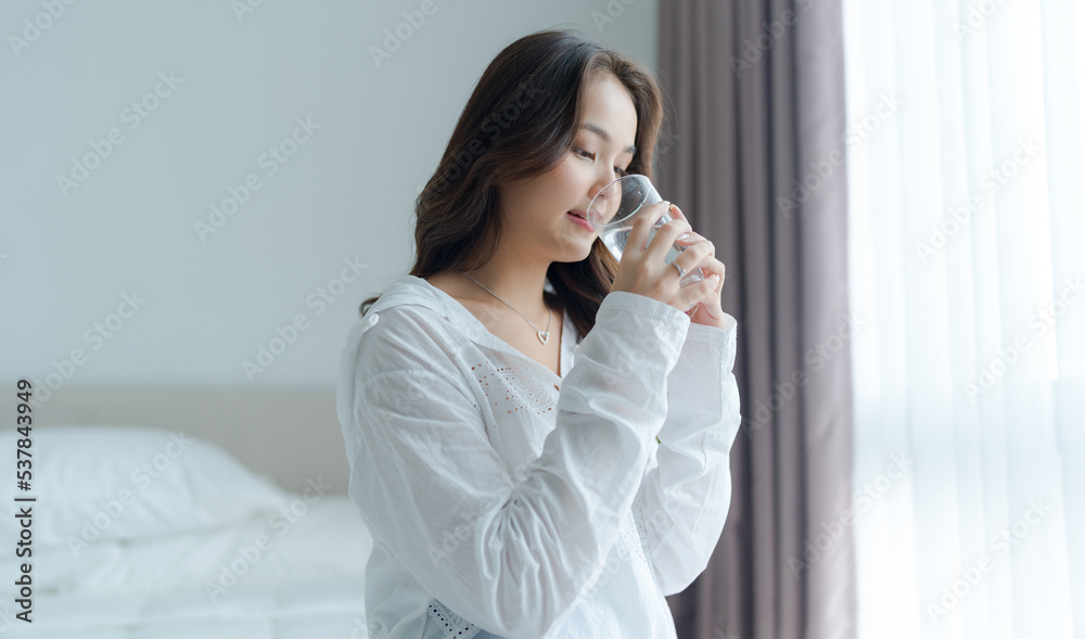 Beautiful girl drinking water and smile happily in the white bedroom. Beautiful girl drinking water and smile happily in the white bedroom.
