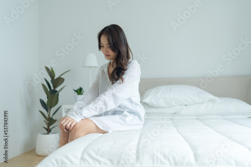 The beautiful girl sat lonely in the bed in the white bedroom.