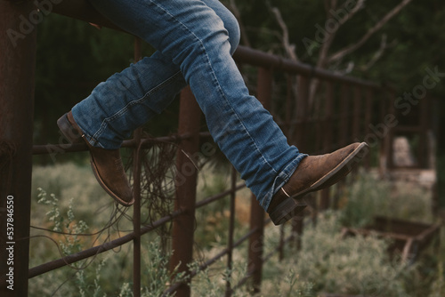 Western lifestyle concept with person sitting on fence in cowboy boots. photo