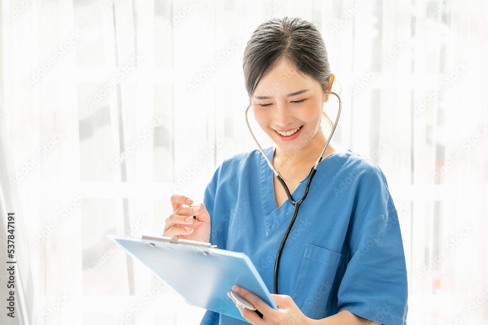Medical concept of confident female doctor in blue medical uniform with stethoscope standing and holding a folder, Asian Woman working in a hospital looking at the report sheet and smiling Medical concept of confident female doctor in blue medical uniform with stethoscope standing and holding a folder, Asian Woman working in a hospital looking at the report sheet and smiling