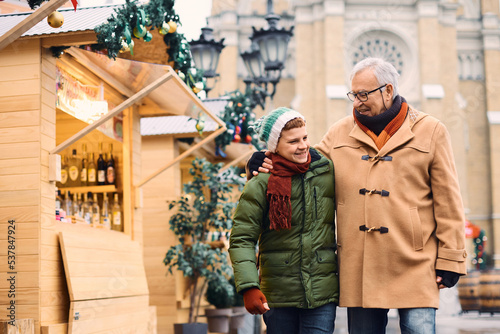 Embraced grandfather and grandson walking through Christmas market during winter holidays. © Drazen