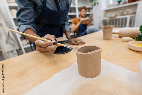 cropped view of african american woman holding shaper while modeling clay cup near blurred man.