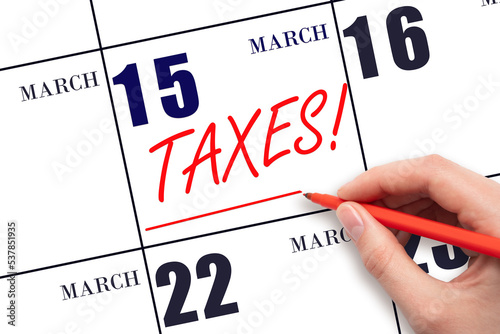 Hand drawing red line and writing the text Taxes on calendar date March 15. Remind date of tax payment