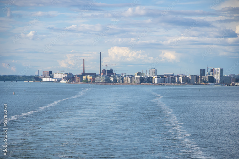 View from the sea to Helsinki skyline on summer evening. Water trail behind ferry in the Baltic sea in the foreground