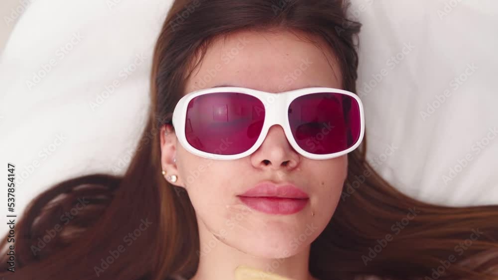 Professional cosmetologist makes a laser facial hair removal to a beautiful woman in a beauty salon. Beautician and spa concept. Body care. Slow motion. Top view. Professional cosmetologist makes a laser facial hair removal to a beautiful woman in a beauty salon. Beautician and spa concept. Body care. Slow motion. Top view.