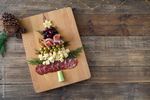 Christmas tree shaped cheese and charcuterie board with wooden background. Top view. Copy space.