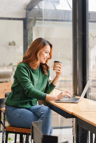 Beautiful Asian girl enjoys coffee while working in a coffee shop on laptop connected to public wifi. Stylish college student studying online while spending free time in the park.