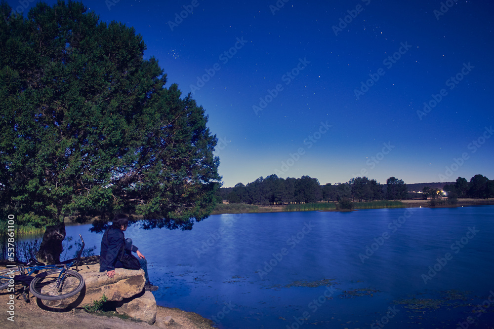 Obraz premium lonely man in a lake at night, sky with stars, and bike next to the young man, lagoon in monte escobedo zacatecas 