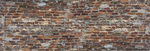 Long old brick wall background with red and orange bricks and holes filled in with concert.