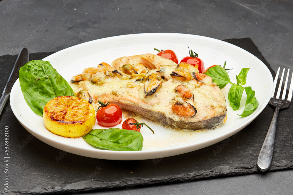 Delicious baked salmon steak with cream sauce and mussels is served on a plate and ready to eat. Restaurant menu position
