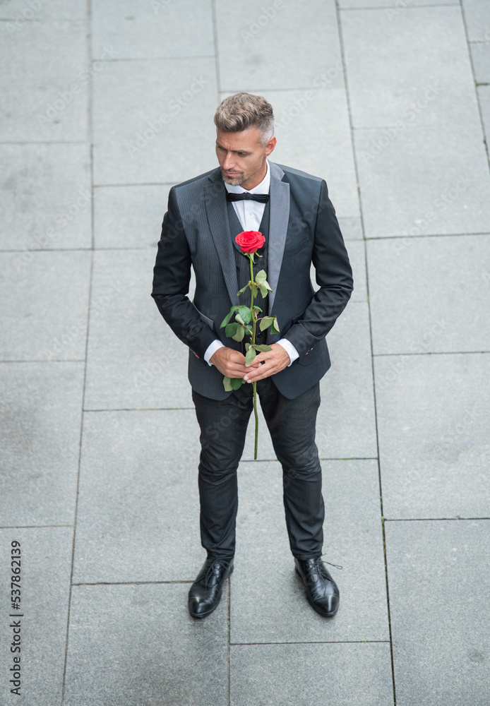elegant man in tuxedo. man wearing bowtie suit outdoor. romantic tuxedo man with red rose elegant man in tuxedo. man wearing bowtie suit outdoor. romantic tuxedo man with red rose