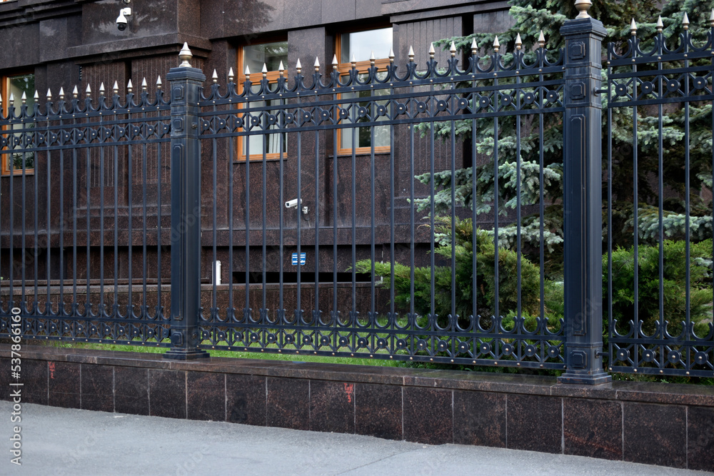 A black iron fence and a red fence with a house in the afternoon. A black iron fence and a red fence with a house in the afternoon.