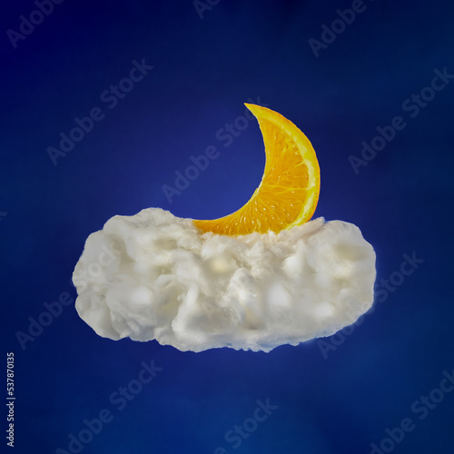 slice of orange like moon liyng down on bright white cloud in the sky on dark blue background. minimal creative composition. photo