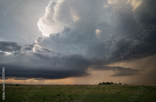 A towering supercell thunderstorm, or cumulonimbus cloud, moves over the prairie near sunset.