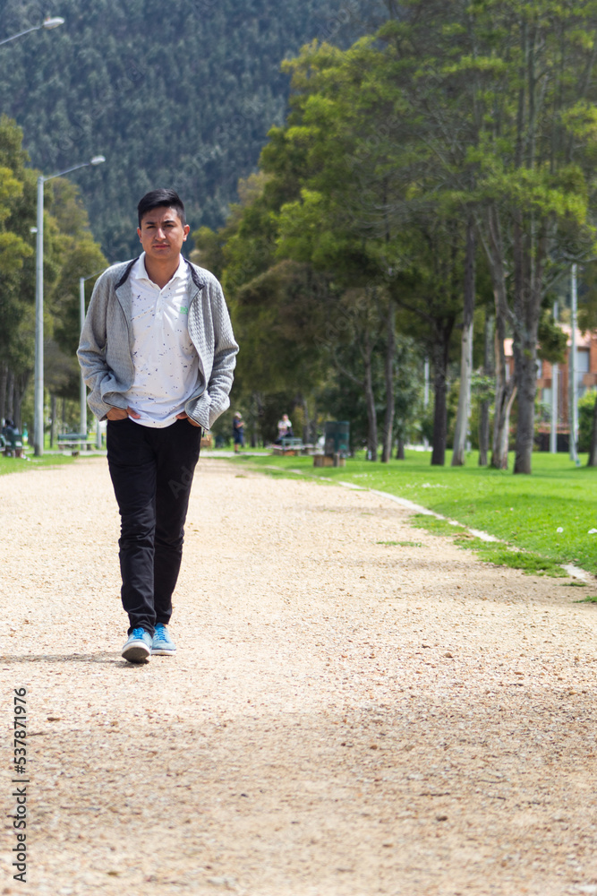 An angry young Latin man walking looking at the camera in the middle of a park on a sunny day