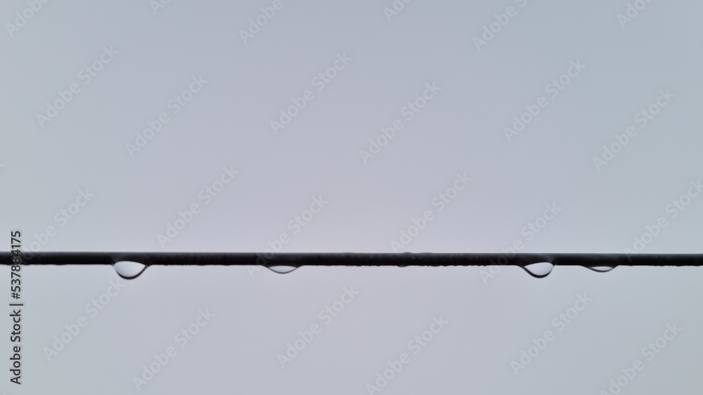 Drops of rain hanging from a cable running across the image on a cold dark grey stormy morning with low lying fog.