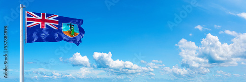 Montserrat flag waving on a blue sky in beautiful clouds - Horizontal banner photo