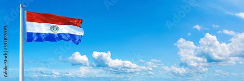 Paraguay flag waving on a blue sky in beautiful clouds - Horizontal banner
